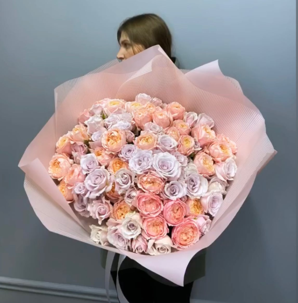 An oversized round bouquet of blush, peach and lavender garden roses wrapped in pleated pink paper