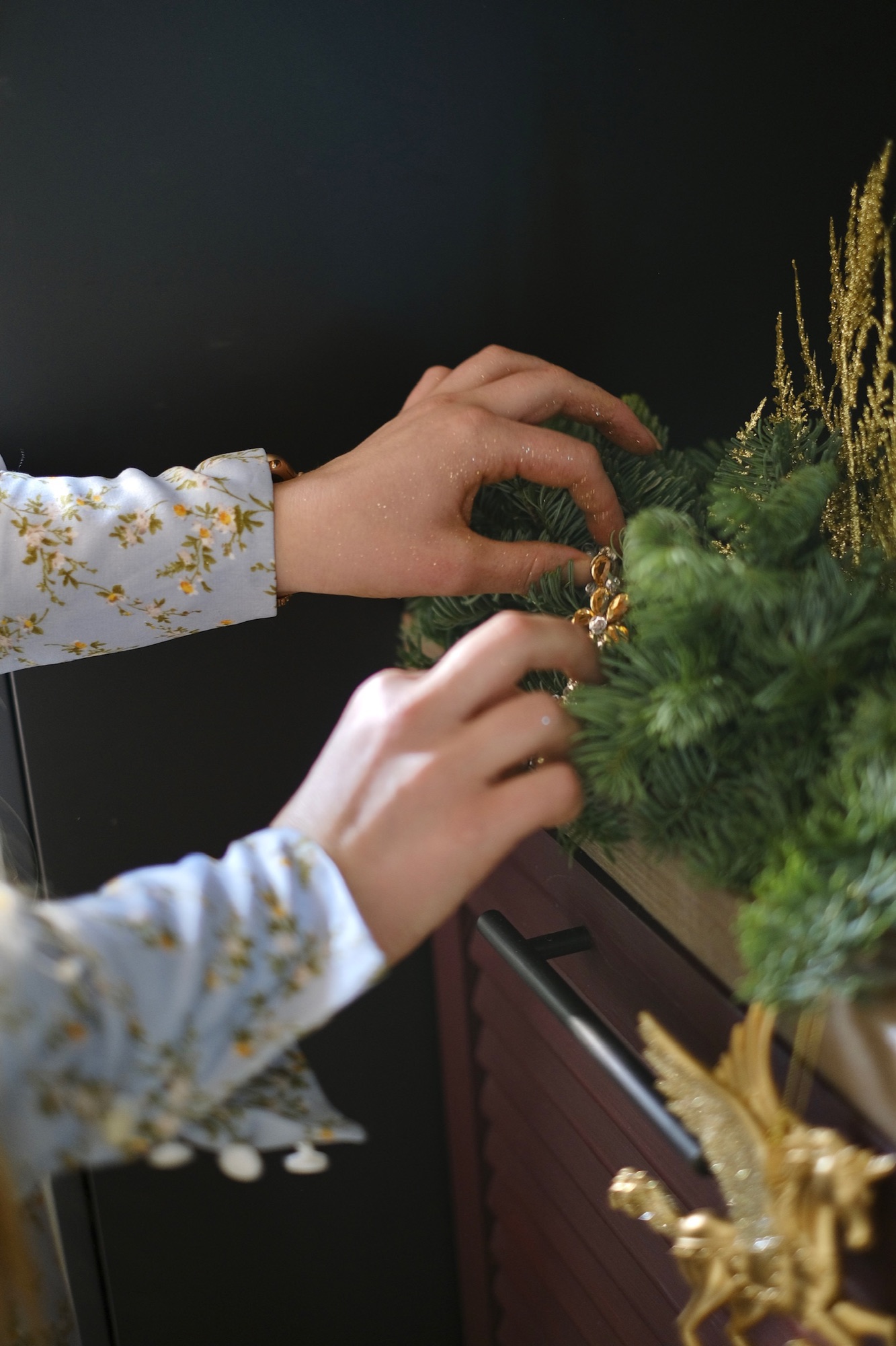 Hands adorning an evergreen garland against a dark background