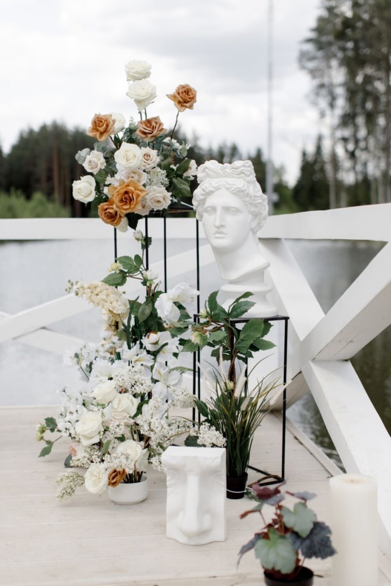 A classical bust styled with roses and greenery on a lakeside deck