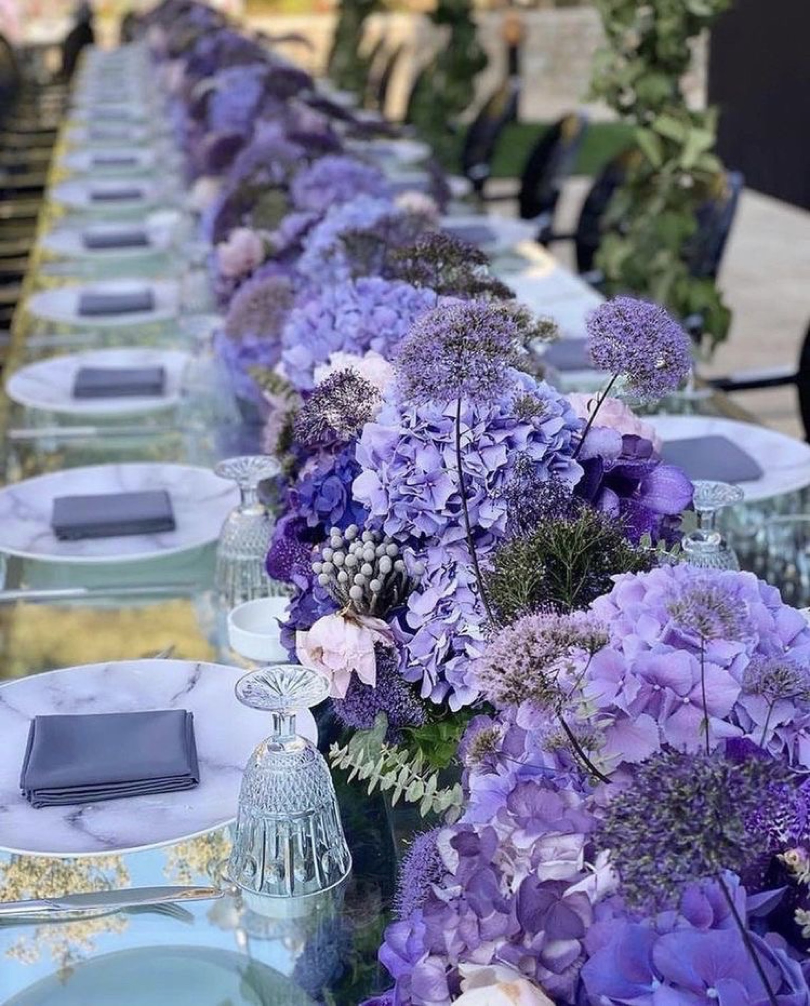 A long dinner table lined with a purple hydrangea and allium runner