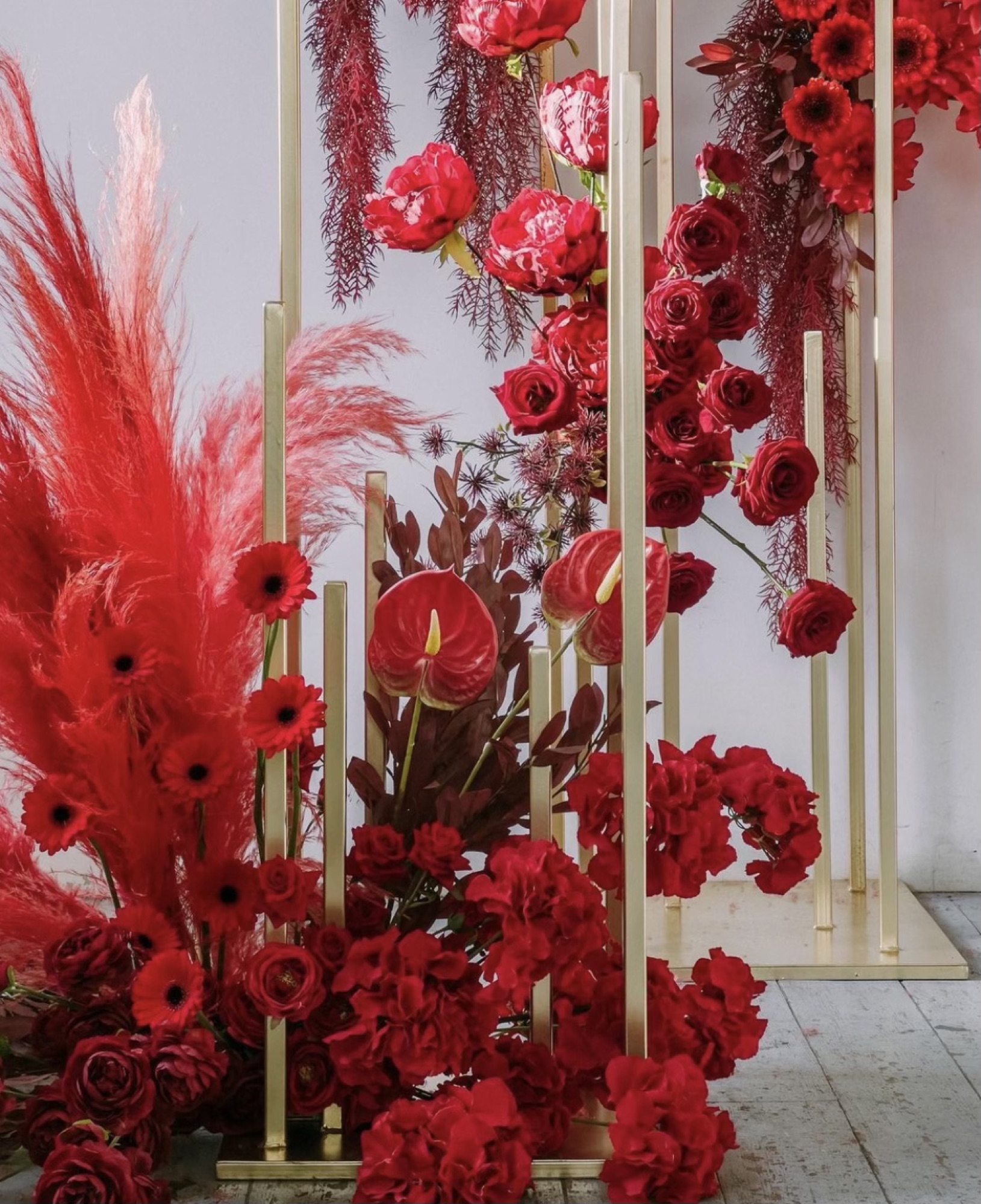 A dramatic red rose and pampas installation on gold stands